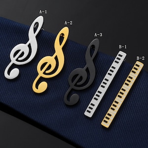 Può includere: Cinque fermagli per cravatta in diversi stili. Tre sono disegni di chiave di violino in argento, oro e nero. Due sono disegni di tasti di pianoforte in argento e oro.