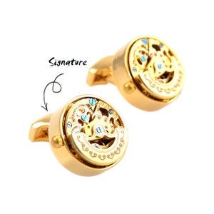 Puede incluir: Gemelos de oro con un diseño de mecanismo de relojería intrincado y giratorio. Los gemelos son una pieza llamativa para cualquier ocasión.