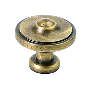 May include: A round, antique brass cabinet knob with a raised centre and a textured finish.