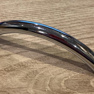 May include: A shiny, silver, curved cabinet handle.