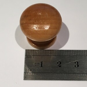 May include: A light brown wooden knob with a diameter of approximately 2.5 cm. The knob is shown next to a ruler for size reference.