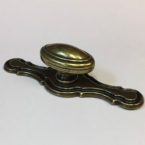 May include: A gold-toned cabinet knob with an oval-shaped handle and a decorative base. The knob has a slightly distressed finish.