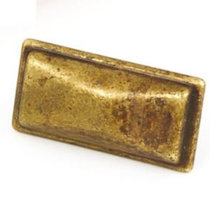 May include: A rectangular brass cabinet pull with a slightly raised, textured centre. The pull has a worn, antique finish.