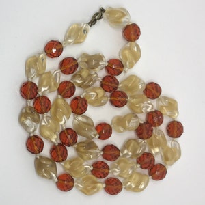 May include: A long necklace made of alternating clear and amber-coloured glass beads. The beads are faceted and have a slightly iridescent finish.