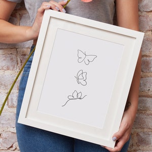 May include: A white framed print with a black line drawing of three butterflies. The butterflies are in different positions, with one flying, one landing, and one on a stem.