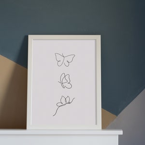 May include: A white framed print with a black line drawing of three butterflies in different positions. The butterflies are drawn in a minimalist style.