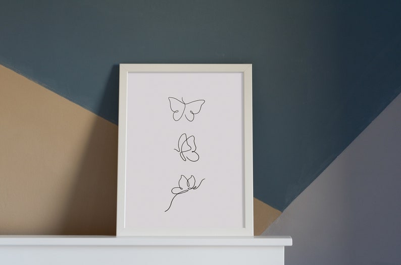 May include: A white framed print with a black line drawing of three butterflies in different positions. The butterflies are drawn in a minimalist style.