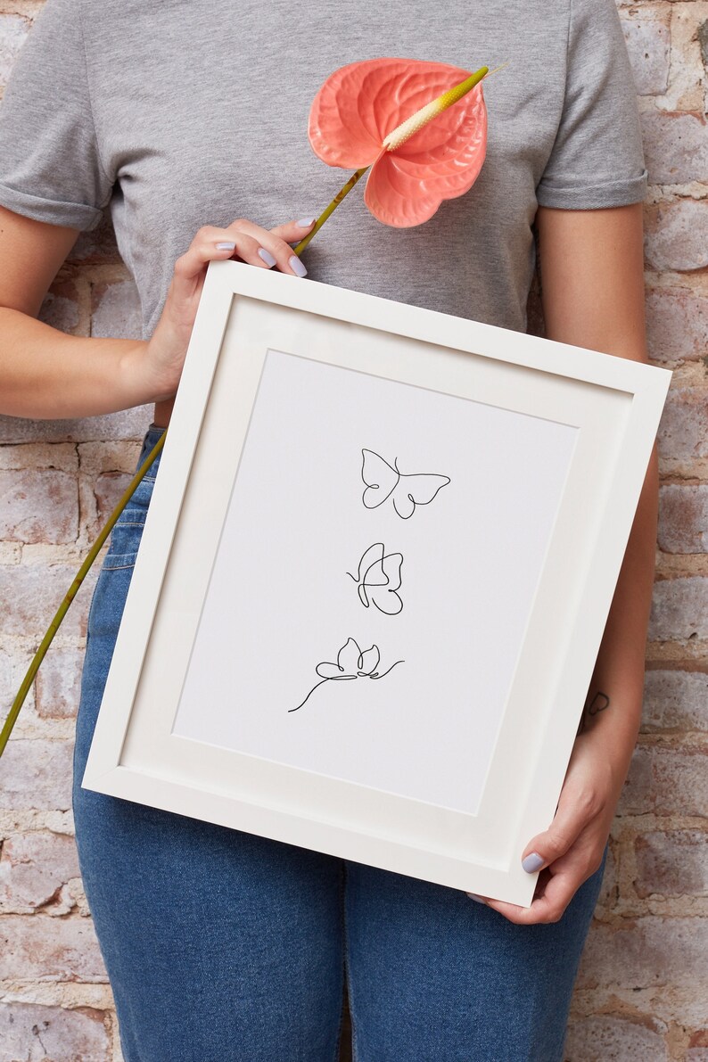 May include: A white framed print with a black line drawing of three butterflies. The butterflies are in different positions, with one flying, one landing, and one on a stem.