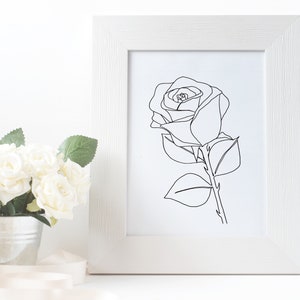 May include: A black and white line drawing of a rose in a white frame. The rose is drawn in a single line, with the stem and leaves also drawn in a single line.