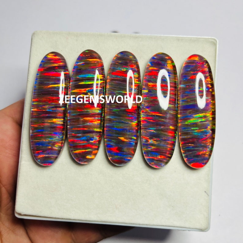 May include: Five oval-shaped opal cabochons with a rainbow of colors, including red, orange, yellow, green, blue, and purple. The opals are set in a white box with the text "EEGENISWORLD" printed on the box.