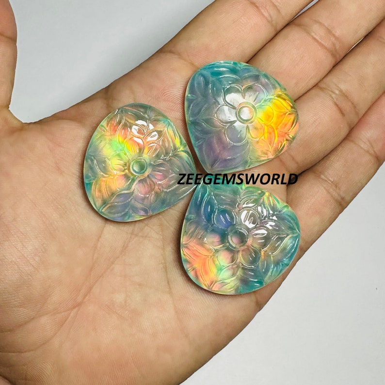 May include: Three iridescent, carved gemstone pendants with a floral design. The pendants are a light blue color with hints of yellow and pink.