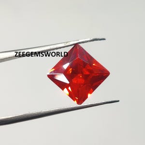 May include: A bright red square-shaped gemstone with a faceted cut. The gemstone is held by tweezers.