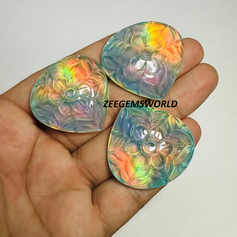 May include: Three iridescent heart-shaped cabochons with carved floral designs. The cabochons are translucent and have a rainbow sheen.
