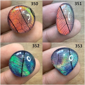 May include: Four iridescent cabochons with leaf vein patterns. The shapes include a circle, oval, and two variations of a teardrop shape. The colors shift from orange to green and blue, with a glossy finish. Each cabochon is labeled with a number.