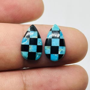 May include: A pair of teardrop-shaped turquoise and black checkerboard inlay cabochons. The cabochons are approximately 2.5 cm in length and have a smooth, polished surface.