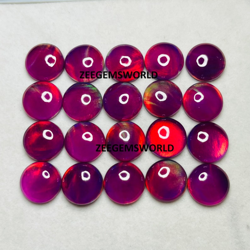 May include: Twenty-four round, iridescent opal cabochons in shades of purple, red, and gold. The cabochons are arranged in four rows of six, with the text "ZEEGEMSWORLD" printed twice on the white background.