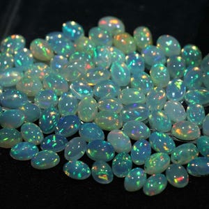 May include: A collection of oval-shaped, iridescent opal gemstones. The opals are a light blue color with flashes of green, yellow, and orange.