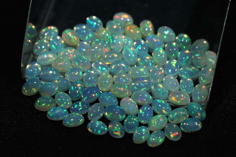 May include: A collection of oval-shaped, iridescent opal gemstones. The opals are a light blue color with flashes of green, yellow, and orange.