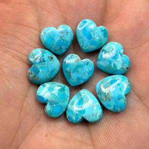 May include: Seven polished heart-shaped turquoise gemstones arranged in a circular pattern. Each stone features a vibrant sky-blue color with natural dark brown matrix veining throughout the smooth, glossy surfaces of the heart-shaped cabochons.