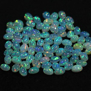 May include: A collection of oval-shaped, iridescent opal gemstones. The opals are a pale white color with flashes of blue, green, and yellow.