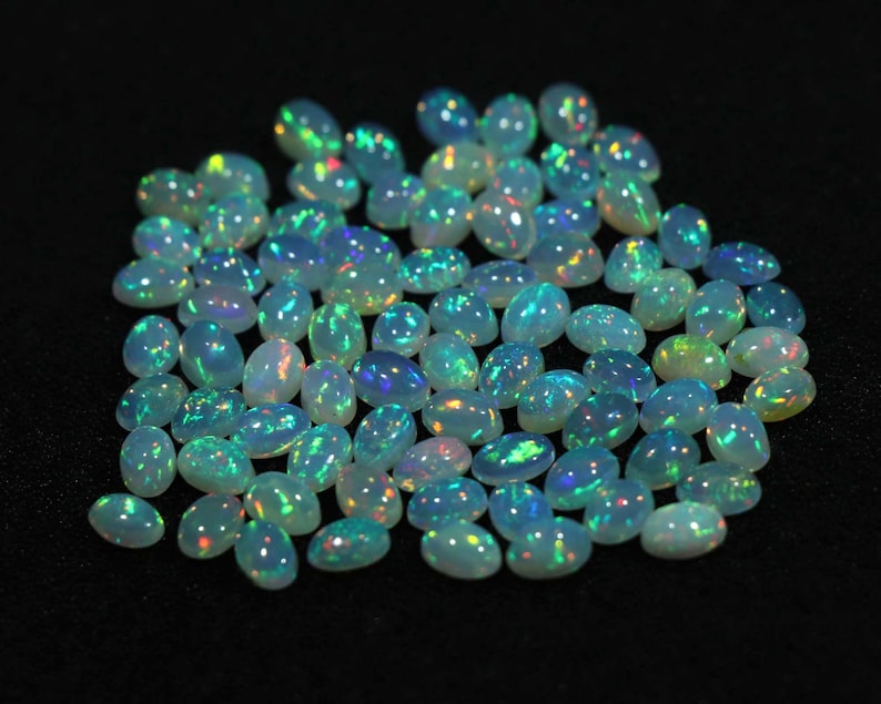 May include: A collection of oval-shaped, iridescent opal gemstones. The opals are a pale white color with flashes of blue, green, and yellow.