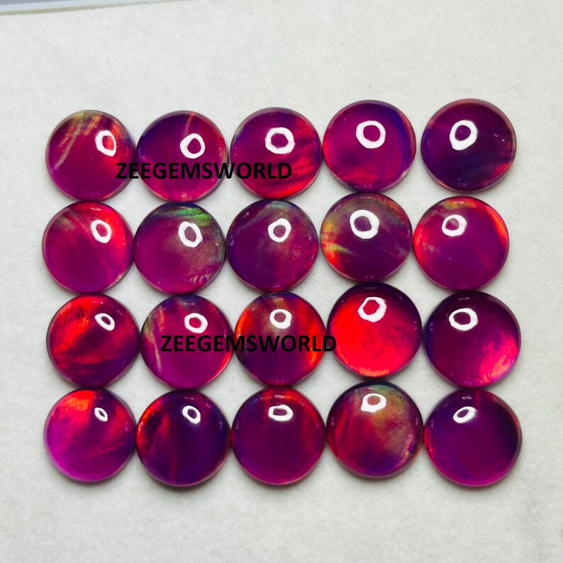 May include: Twenty-four round, iridescent cabochons in shades of purple, red, and orange. The cabochons are arranged in four rows of six. The text "Zeegemsworld" appears twice in the image.
