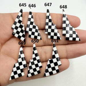 May include: A collection of nine black and white checkered flag-shaped nail art decorations. Each piece has a pointed top and a jagged edge, with the numbers 645 through 651 and 648 and 649 printed on them.