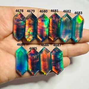 Op de afbeelding: Een verzameling van 10 iriserende, gefacetteerde, achthoekige glazen cabochons. De cabochons zijn gerangschikt in twee rijen, met de nummers 4678 tot en met 4687 gedrukt boven elke steen.