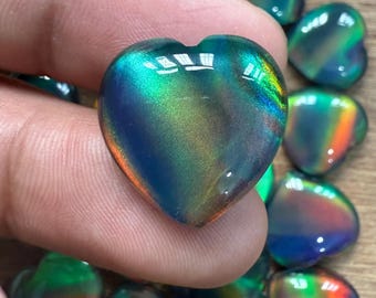 Op de afbeelding: Een verzameling hartvormige edelstenen met een glanzend, iriserend uiterlijk. De stenen tonen een scala aan kleuren, waaronder blauw, groen en oranje, met een glanzende afwerking. De hartvormen zijn uniform.