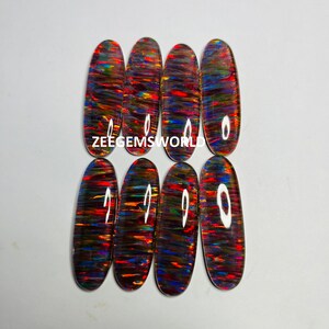 May include: Seven oval-shaped, iridescent opal cabochons with a rainbow of colors, including red, orange, yellow, green, blue, and purple. The cabochons are arranged in two rows, with the text "ZEEGEMS WORLD" printed below the top row.