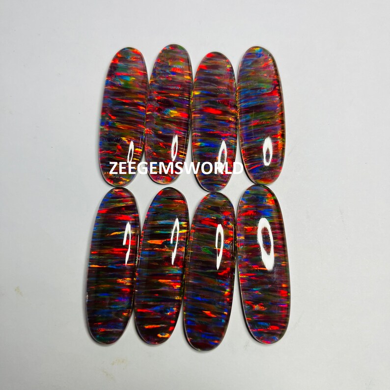 May include: Seven oval-shaped, iridescent opal cabochons with a rainbow of colors, including red, orange, yellow, green, blue, and purple. The cabochons are arranged in two rows, with the text "ZEEGEMS WORLD" printed below the top row.