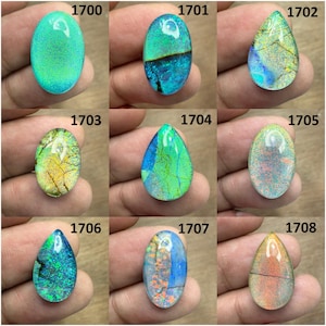 May include: Nine polished opal gemstones in various shapes and colors. The opals range from oval to teardrop, with vibrant hues of green, blue, yellow, and orange. Each stone has unique internal patterns and cracks.