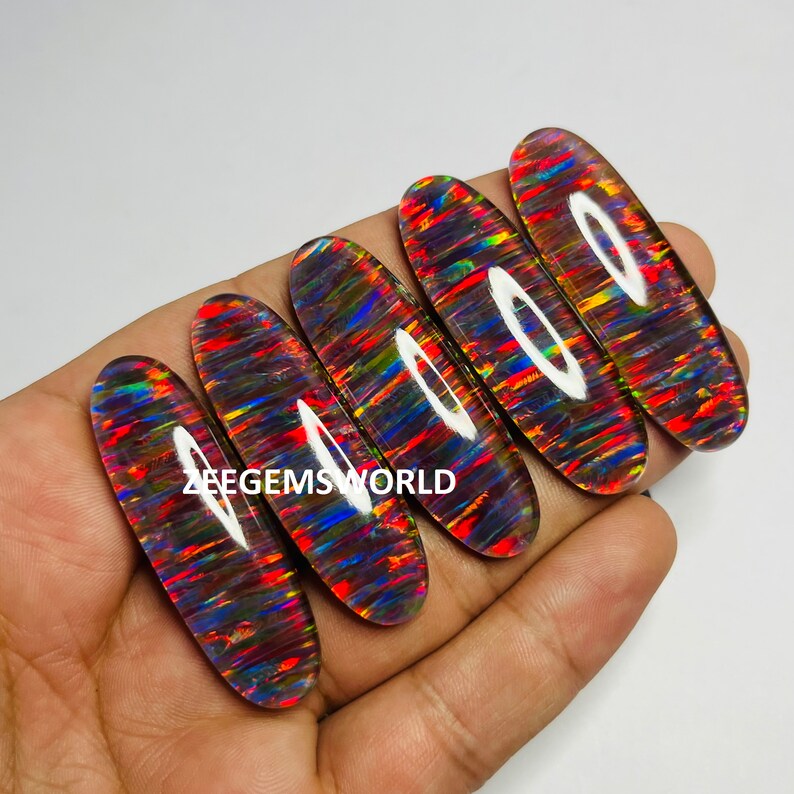 May include: Five oval-shaped, iridescent opal cabochons with a rainbow of colors, including red, orange, yellow, green, blue, and purple. The opals are set against a dark background.