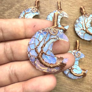 May include: Handmade crescent moon pendant necklaces. Each pendant features a light blue and white opal-like stone, intricately wrapped with copper wire in a tree-like design. The pendants are displayed on a wooden surface.