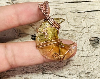 May include: A crescent moon shaped pendant made from clear, amber-colored glass wrapped with copper wire. The pendant has a copper wire bail.