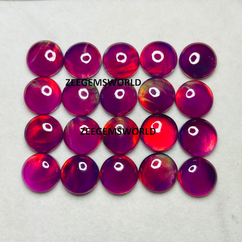 May include: Twenty-four round, iridescent cabochons in shades of purple, red, and gold. The cabochons are arranged in four rows of six. The text "Zeegemsworld" appears twice on the image.