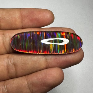 Pu&ograve; includere: Un cabochon di opale vibrante, multicolore, con un motivo ad anello bianco. L'opale ha una base scura con bagliori di rosso, arancione, giallo, verde, blu e viola.
