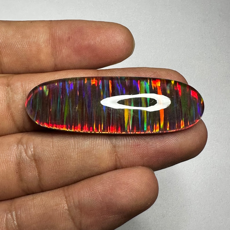 Pu&ograve; includere: Un cabochon di opale vibrante, multicolore, con un motivo ad anello bianco. L'opale ha una base scura con bagliori di rosso, arancione, giallo, verde, blu e viola.