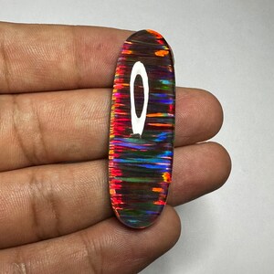 Pu&ograve; includere: Un cabochon di opale ovale e colorato con un arcobaleno di colori, tra cui rosso, arancione, giallo, verde, blu e viola. L'opale ha un lampo bianco al centro.
