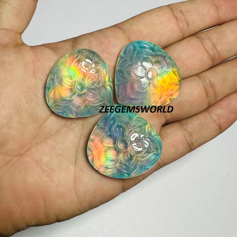 May include: Three iridescent, carved gemstone cabochons in the shape of a flower. The cabochons are a light blue color with a rainbow sheen.