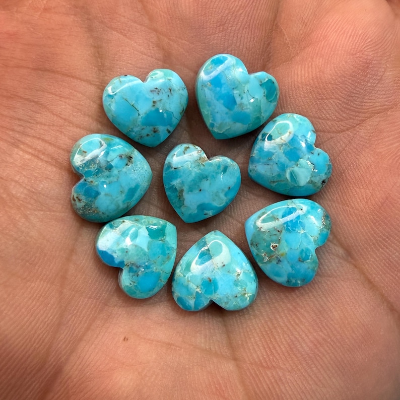 May include: Seven small, heart-shaped turquoise gemstones with a polished, smooth finish. Each stone displays a vibrant sky-blue color with intricate, dark brown matrix veining patterns throughout the surface, arranged in a circular cluster.