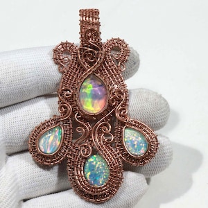 May include: A copper wire wrapped pendant featuring three iridescent opal stones. The pendant is shaped like a teardrop with a smaller teardrop on each side.
