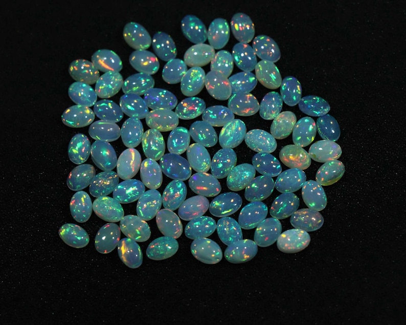 May include: A collection of oval-shaped opal gemstones with iridescent colors, including blue, green, and red.