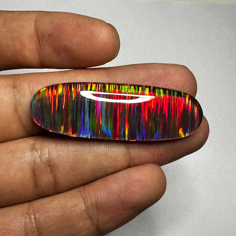 Pu&ograve; includere: Un cabochon di opale vibrante e multicolore con un arcobaleno di colori, tra cui rosso, arancione, giallo, verde, blu e viola. L'opale ha un motivo striato unico ed &egrave; incastonato in una montatura d'argento.
