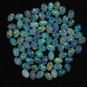May include: A collection of oval-shaped, iridescent opal gemstones. The opals are a light blue color with flashes of green, yellow, and red.