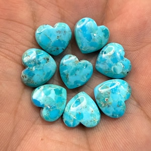 May include: Seven small heart-shaped turquoise stones with a bright blue color and natural brown matrix veining. Each stone features a smooth, polished surface with a glossy finish, arranged in a circular pattern on a skin-toned surface.