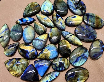Könnte beinhalten: Eine Sammlung von 20 Labradorit-Edelsteinen in verschiedenen Blautönen, Grüntönen und Goldtönen. Die Cabochons sind alle birnenförmig und haben eine glatte, polierte Oberfläche.