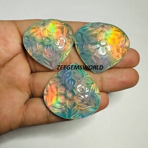 May include: Three iridescent, carved gemstone pendants in the shape of a heart with a floral design. The gemstones are a pale green color with a rainbow sheen.