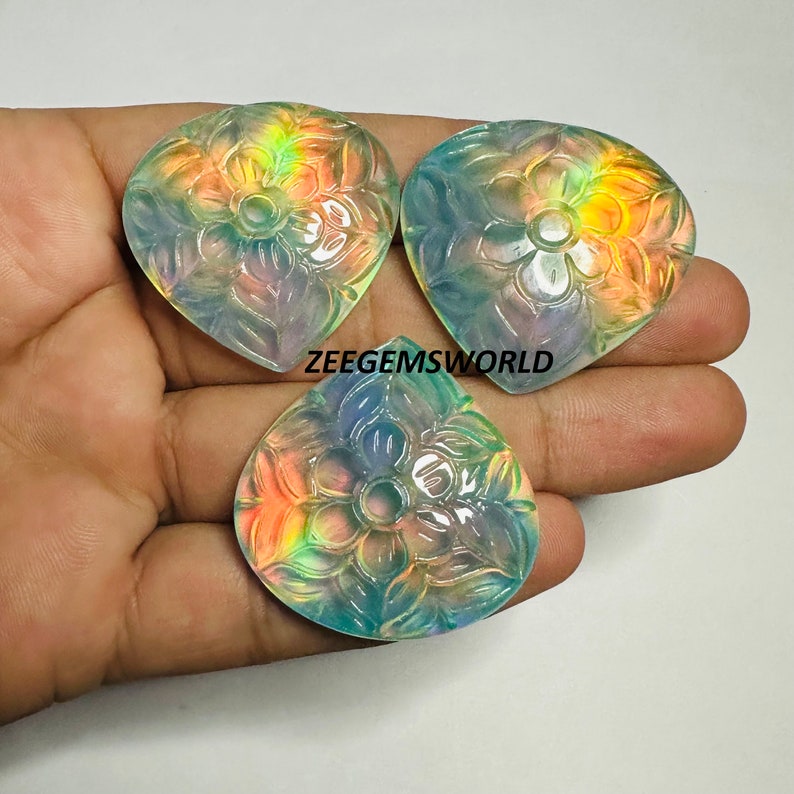 May include: Three iridescent, carved gemstone pendants in the shape of a heart with a floral design. The gemstones are a pale green color with a rainbow sheen.