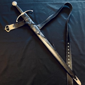 May include: A medieval sword with a black leather scabbard and belt. The sword has a silver crossguard and pommel, with a black handle. The scabbard is detailed with leather wrappings and a gold-coloured buckle. The sword is shown against a dark background.